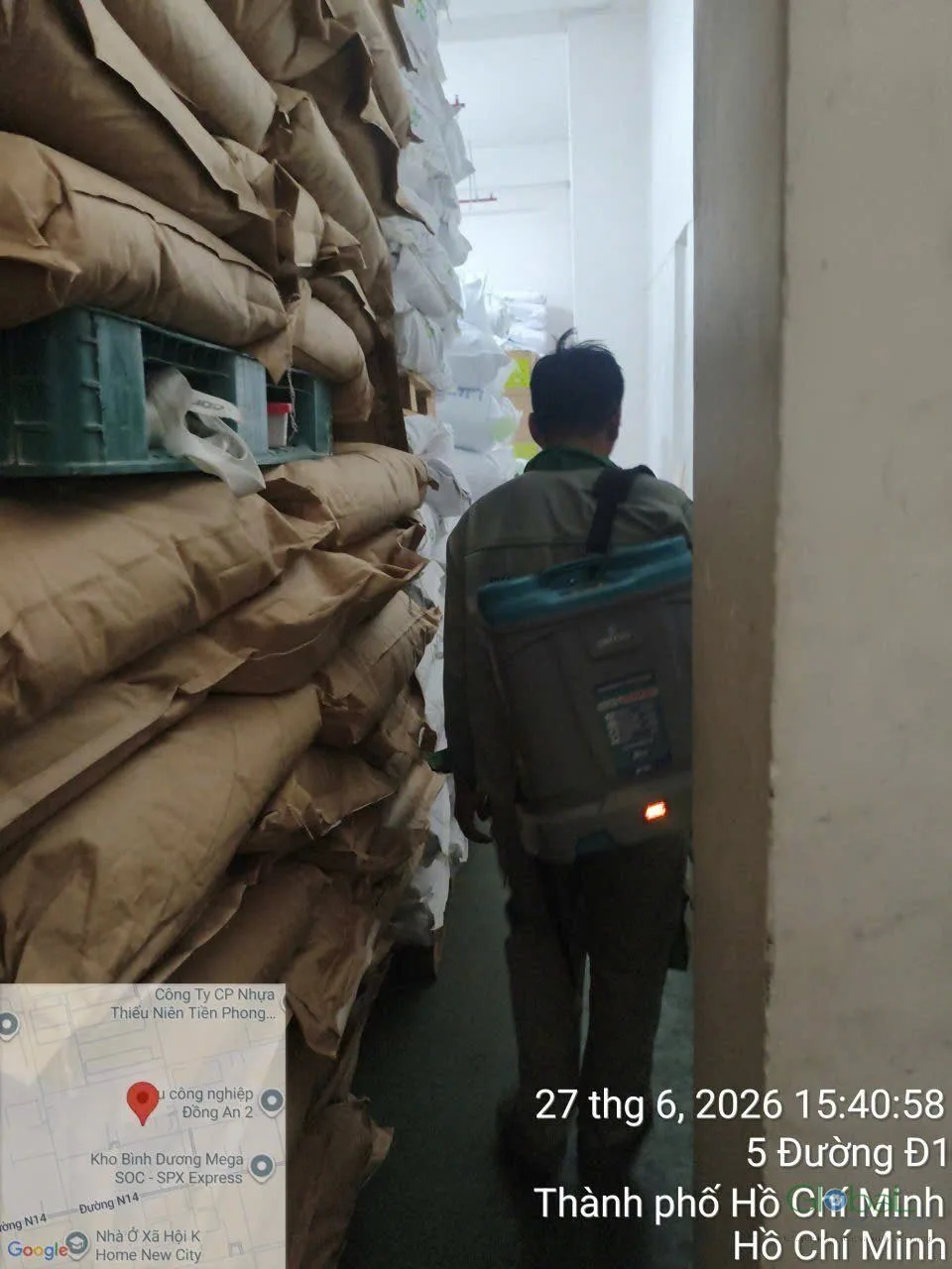 Kỹ thuật viên phun thuốc kẽ pallet bao nguyên liệu trong kho
