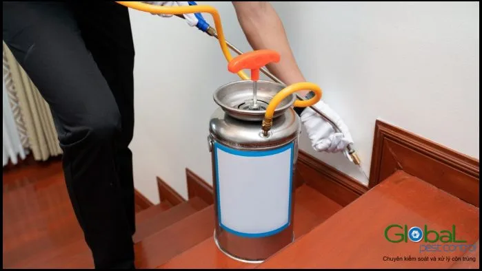 Kỹ thuật viên phun thuốc chân tường cầu thang gỗ bằng bình phun cầm tay